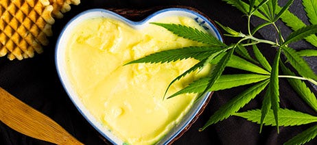 Cannabis butter in a heart shaped tin next to cannabis leaves