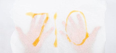 "710" spelled out in cannabis oil on a white sheet held up by two hands