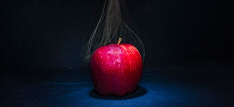 Red apple on a black background with grey smoke wafting from the top