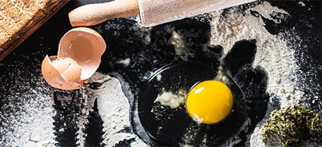 Raw egg and flower on a black surface with a rolling pin