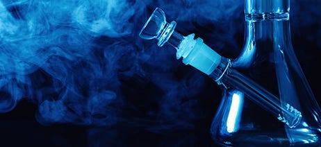 Bottom half of a glass bong with smoke swirling in the background