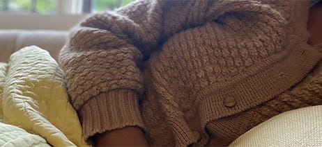 Woman in brown cardigan laying down with a cream colored blanket