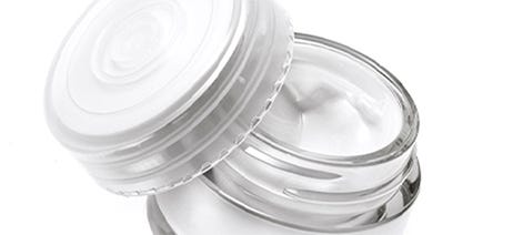 Small glass jar of white cream on a white background