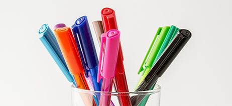 Colorful pens in a clear cup sitting on a table