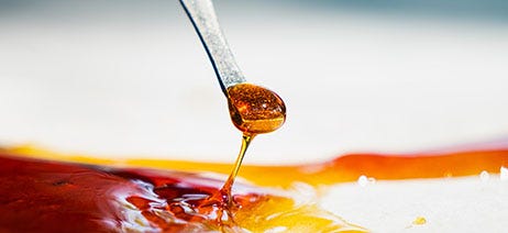 Cannabis resin being scooped on a dab tool and dropping down onto parchment paper