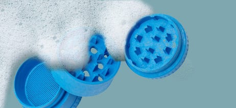 Blue three-part cannabis grinder soaking in water with bubbles on top