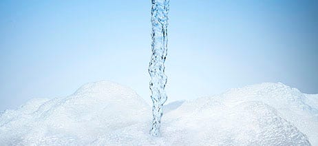 Stream of water on a blue background pouring into a pile of soap bubbles