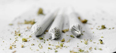 Three marijuana infused pre-rolls with small nuggets of flower sprinkled around them