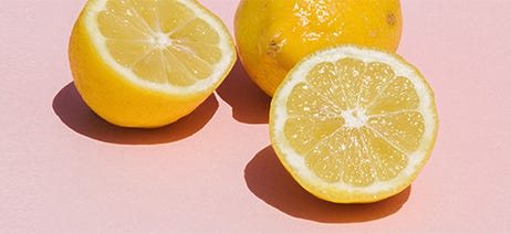 One whole lemon and a lemon sliced in half on a pink background