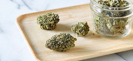 Jar of cannabis flower and cannabis buds on a light wooden rolling tray