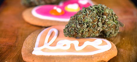 Heart-shaped cookie with love written on it in white icing and a cannabis bud sitting on top