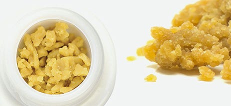 Cannabis crumble in a white jar next to a pile of crumble