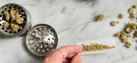 Hands rolling a pre-roll next to a grinder with cannabis flower inside