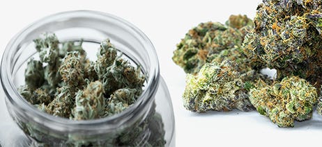 Premium flower in a clear jar next to a pile of cannabis flower