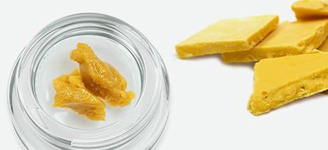 Cannabis wax in a clear jar next to a pile of cannabis wax