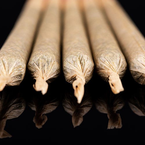 Five cannabis joints laying next to reach other on a black table