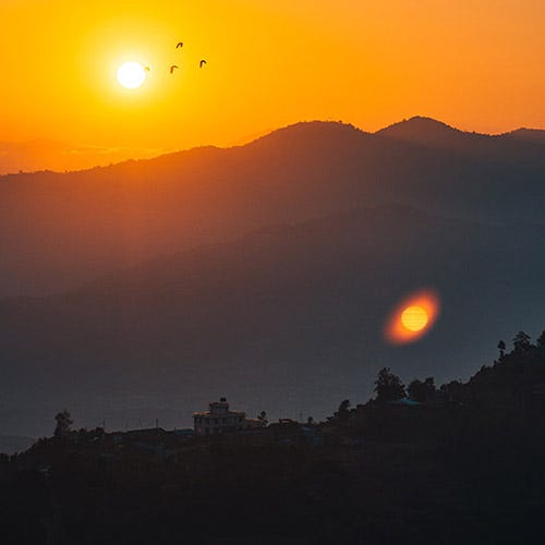 Mountains with the sun setting behind them and birds flying overhead