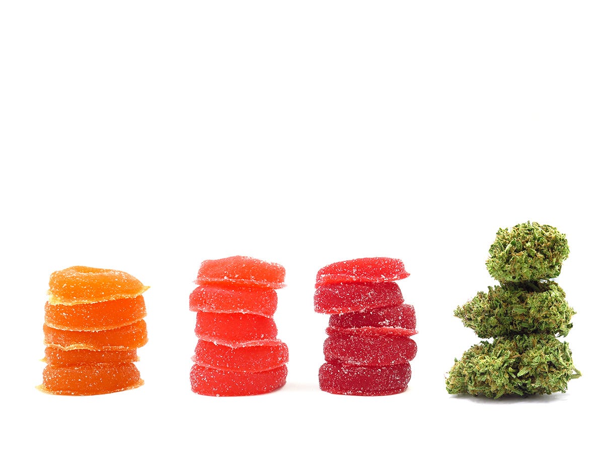 Three stacks of colorful gummies next to a cannabis flower bud