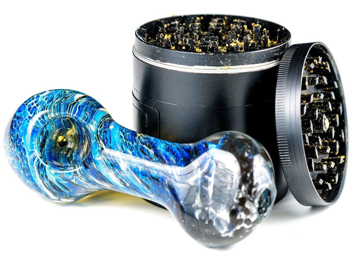 Blue glass hand pipe next to a grinder with the lid resting next to it
