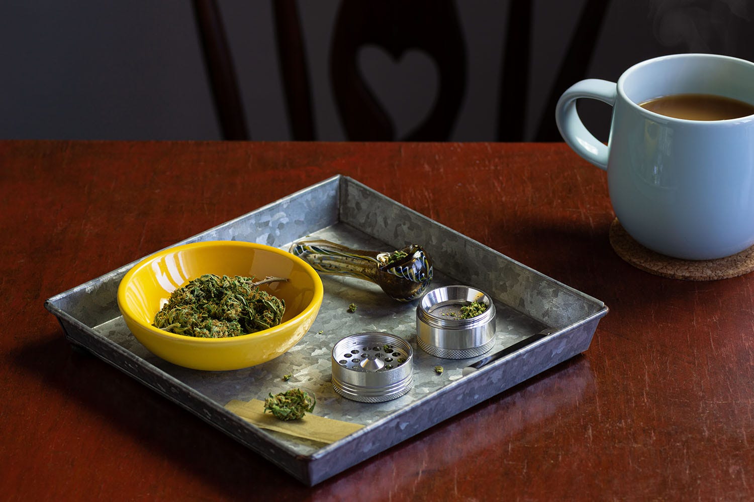 Metal rolling tray holding a glass marijuana pipe, a metal grinder, and a yellow bowl of cannabis flower