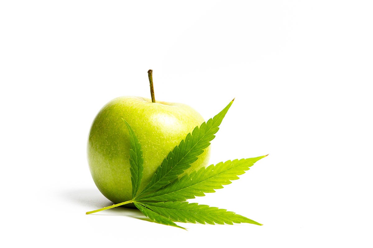 Green apple sitting on top of a cannabis fan leaf