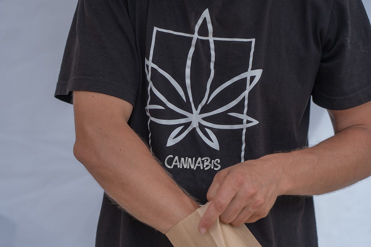 A person wearing a cannabis shirt putting items in a brown bag