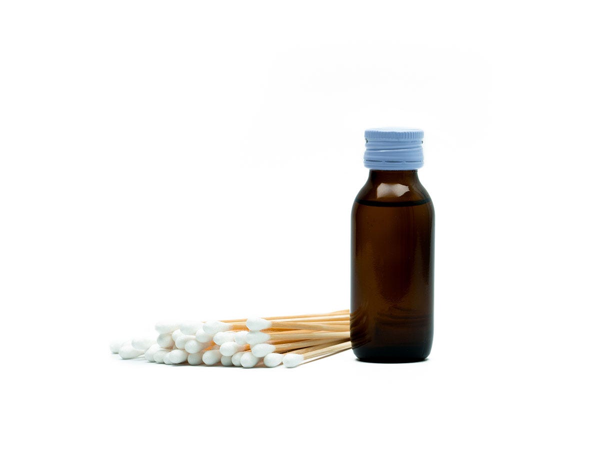 Opaque medical alcohol bottle next to a pile of cotton swabs