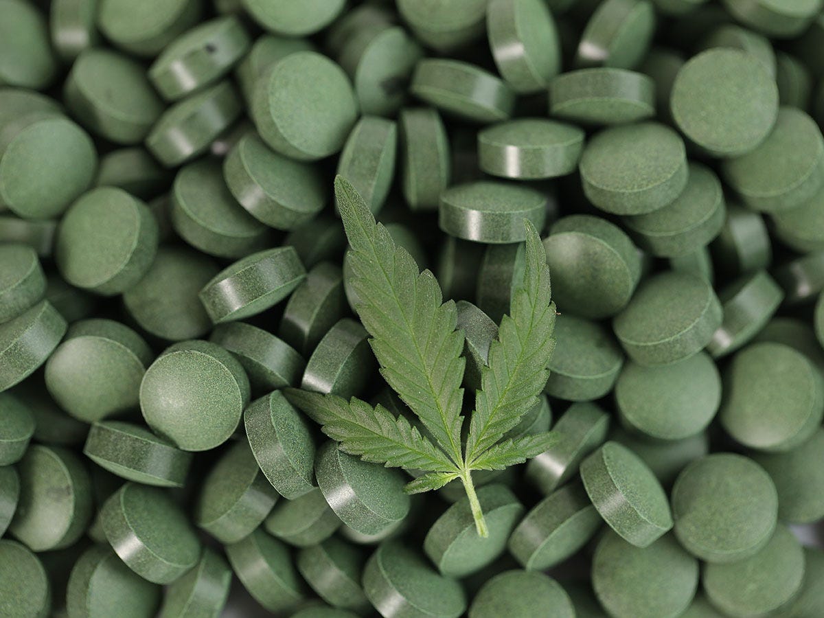 Cannabis leaf on top of a pile of green tablets