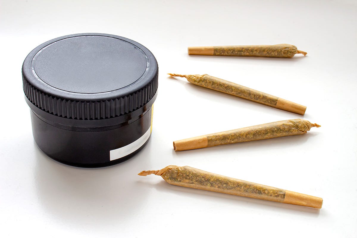 Black cannabis flower jar next to four pre-rolls