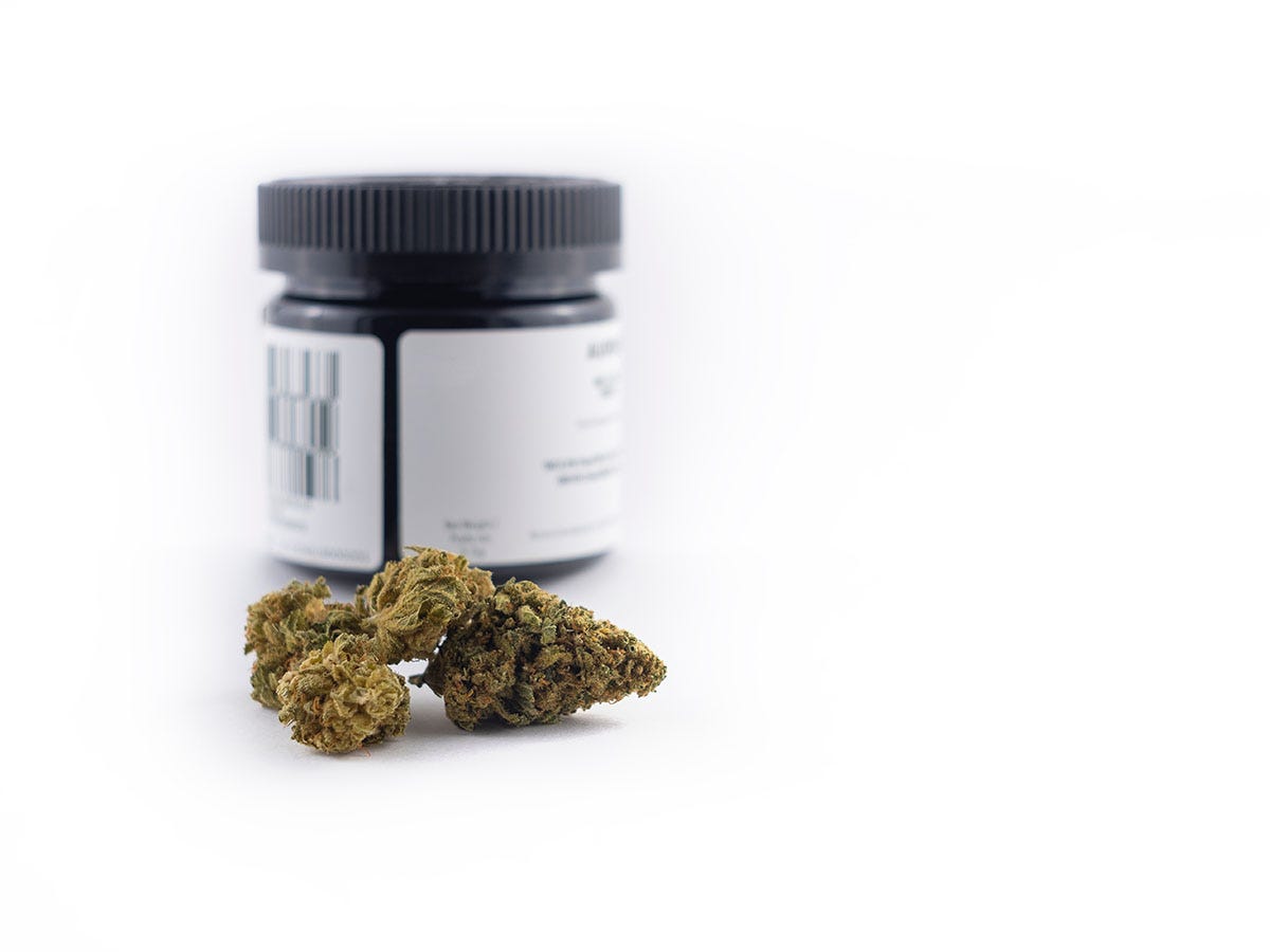 Jar of cannabis with a flower bud in front of it