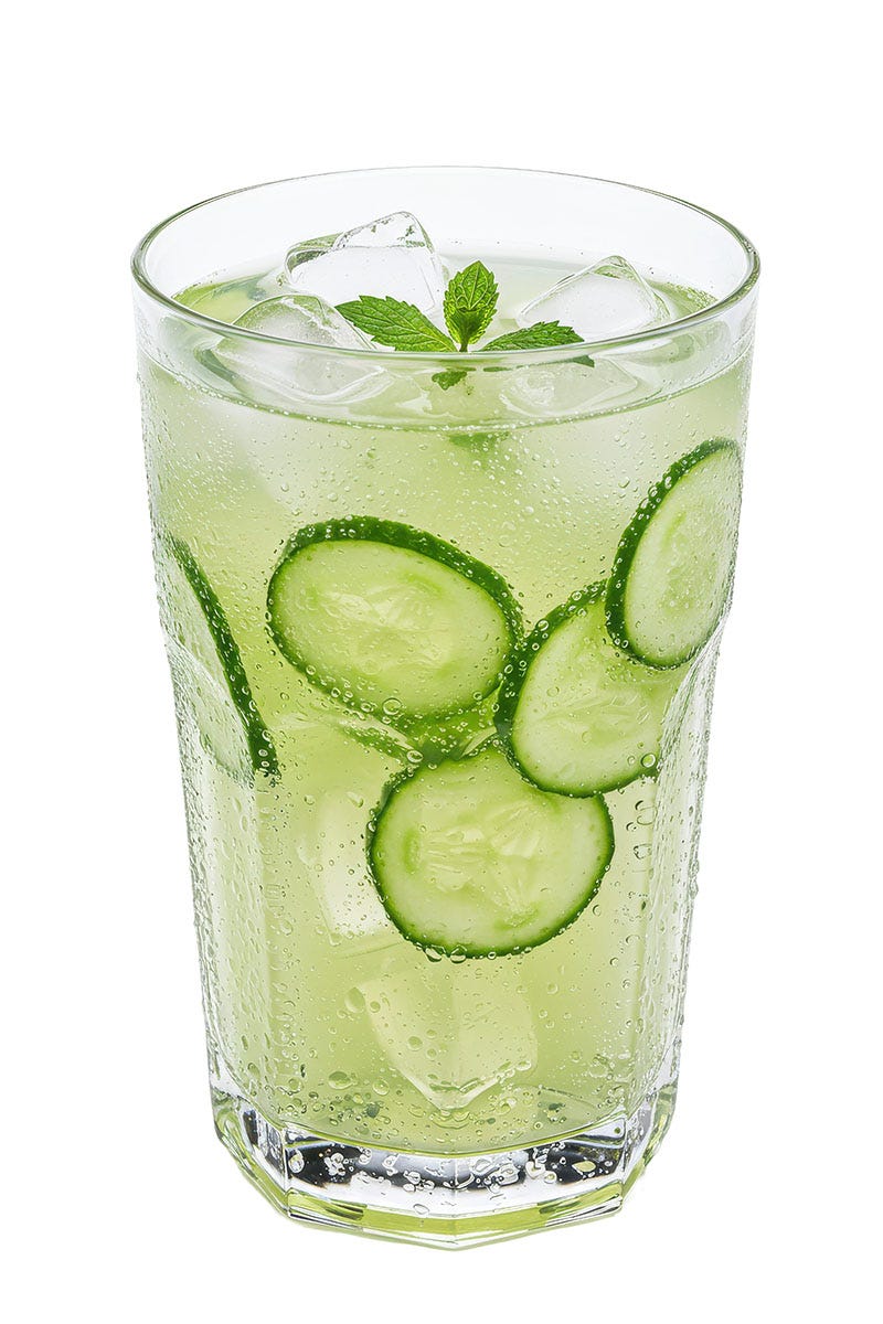 Fizzy green liquid in a clear glass with mint and cucumbers floating inside
