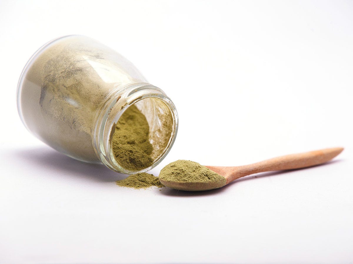 An overturned jar spills green-tinted THC powder on a white background