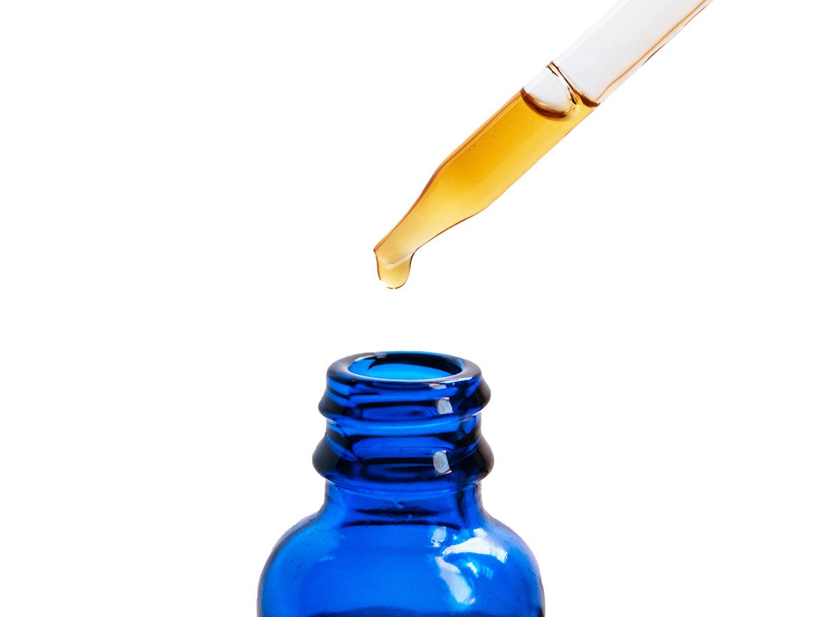 Eye dropper dropping amber liquid into a blue medicine bottle