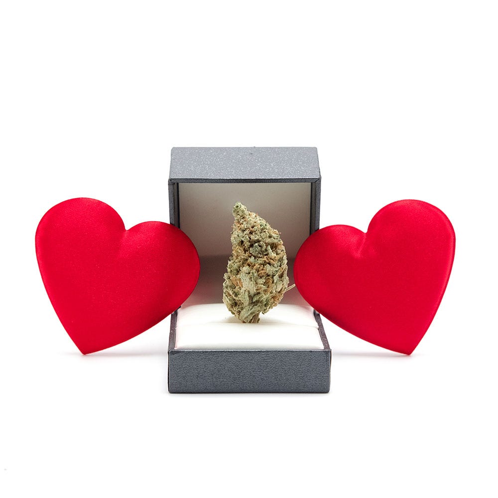 Cannabis flower in a ring box surrounded by two large hearts